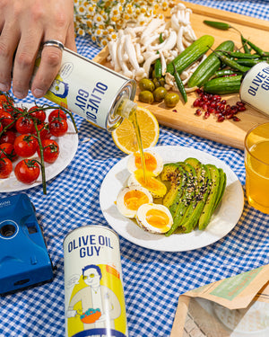 Olive Oil Guy olive oil being poured over a salad on a checkered tablecloth.