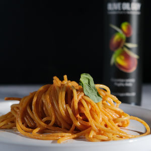 Spaghetti dish with a basil leaf on a white plate, with a bottle of olive oil in the background.